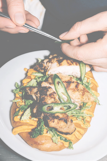 Chef using tweezers to garnish a chicken flatbread with jalapeno slices