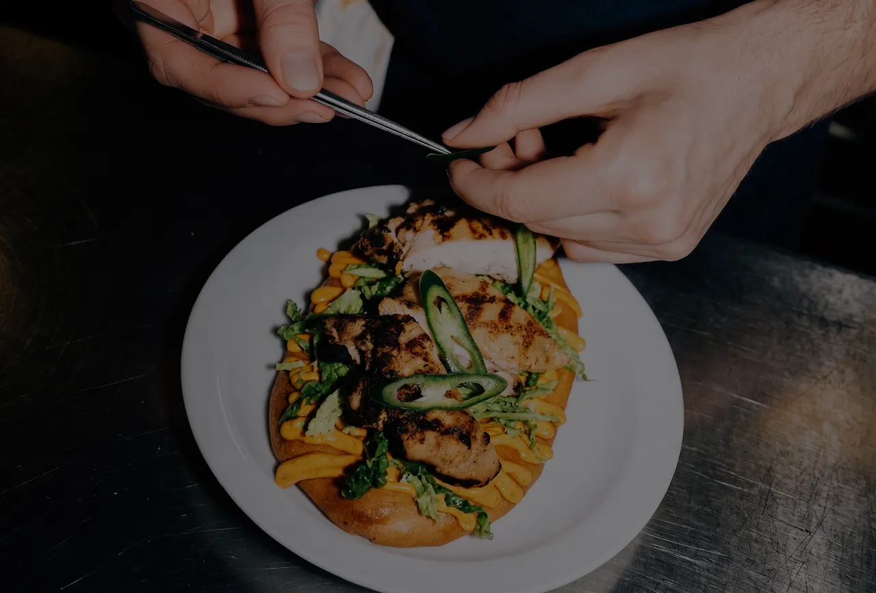 Chef using tweezers to garnish a chicken flatbread with jalapeno slices
